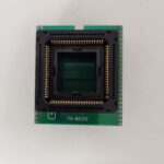 A green circuit board with a central black chip socket.